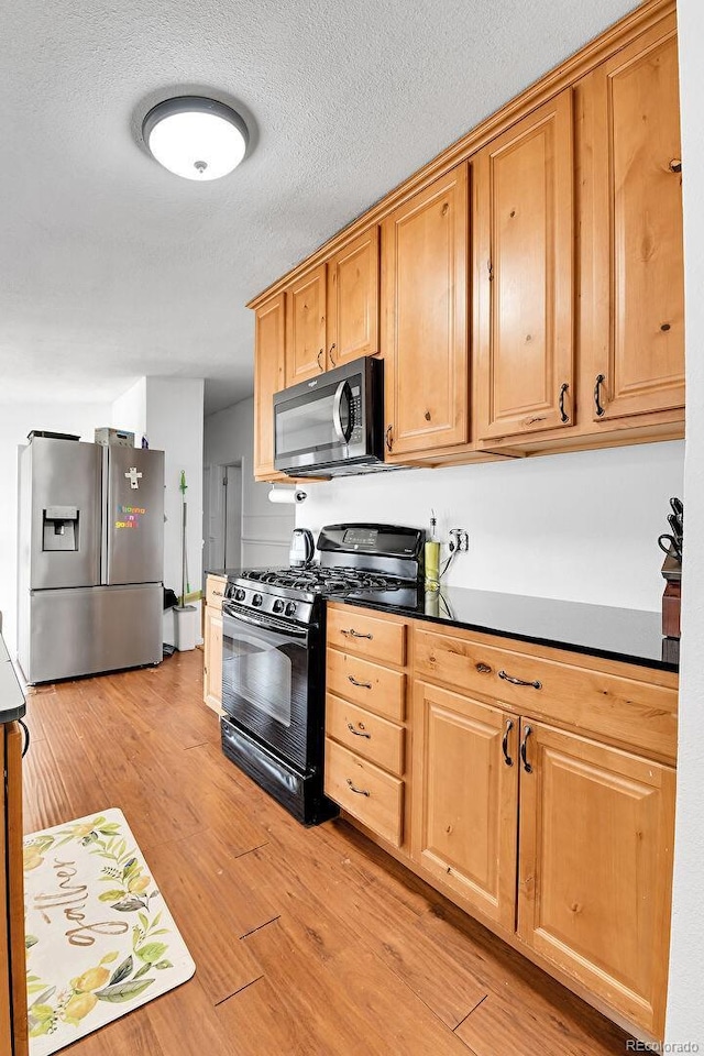 2580 Valley View Dr, Denver, CO 80221 - kitchen with black gas range, stainless steel fridge, light wood-style floors, dark countertops, and a textured ceiling