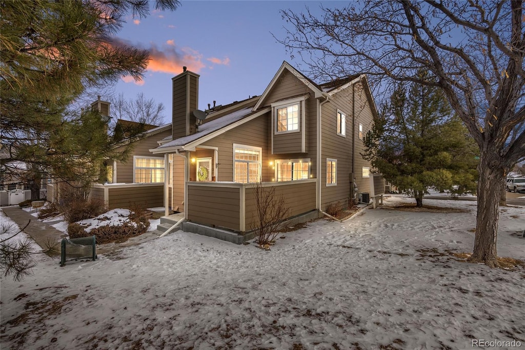 snow covered rear of property with cooling unit and a chimney