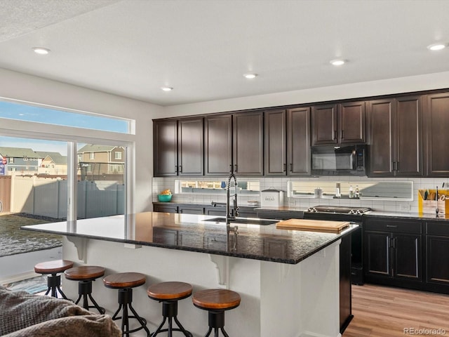 kitchen with a kitchen island with sink, sink, decorative backsplash, and dark stone countertops