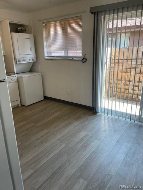 clothes washing area with stacked washer / dryer, light wood-style flooring, and baseboards