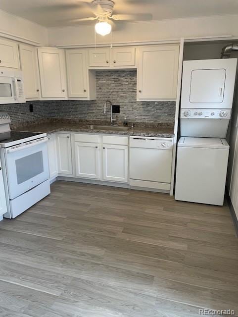kitchen featuring white appliances, estacked washer and dryer, a sink, decorative backsplash, and a ceiling fan
