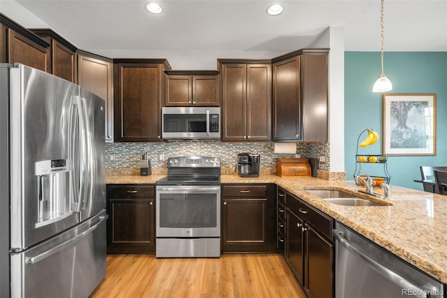 kitchen with backsplash, appliances with stainless steel finishes, light wood-type flooring, dark brown cabinets, and light stone counters