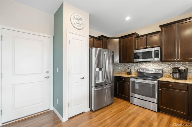 kitchen featuring dark brown cabinets, appliances with stainless steel finishes, light stone counters, light wood-style flooring, and backsplash