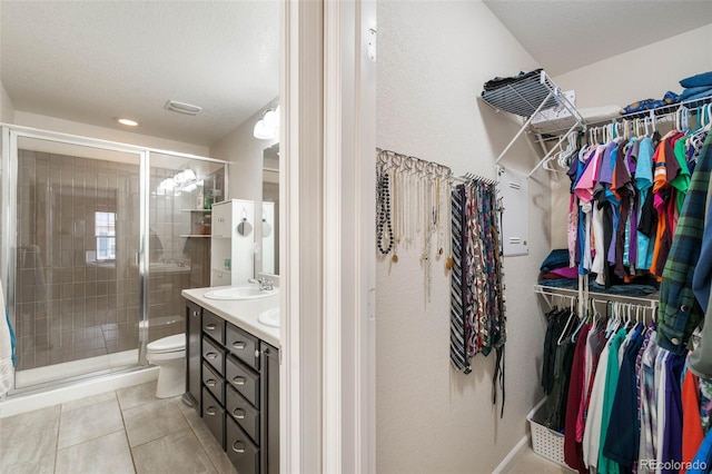 bathroom with vanity, toilet, a walk in closet, tile patterned floors, and a stall shower