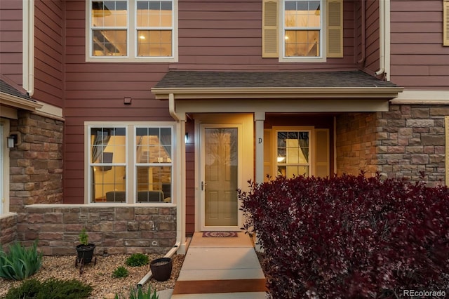 entrance to property featuring covered porch, roof with shingles, and stone siding
