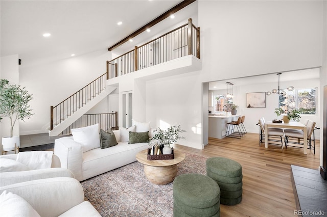 living room with a notable chandelier, beamed ceiling, a high ceiling, and hardwood / wood-style flooring