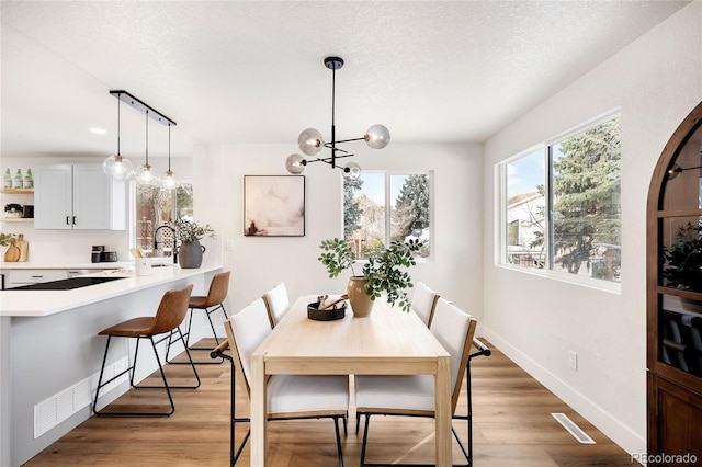 dining area with a textured ceiling, light hardwood / wood-style flooring, and an inviting chandelier