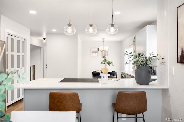 kitchen featuring hardwood / wood-style floors, pendant lighting, a kitchen bar, kitchen peninsula, and white cabinetry