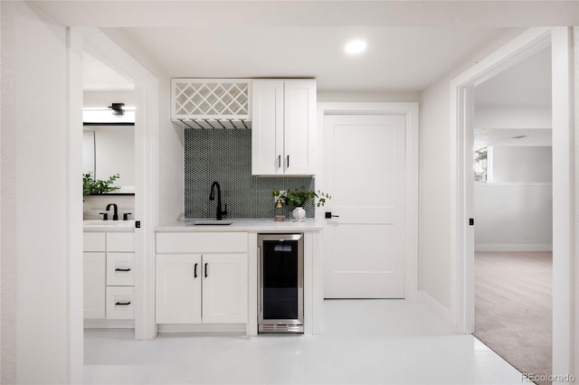 bar featuring wine cooler, light colored carpet, tasteful backsplash, sink, and white cabinets