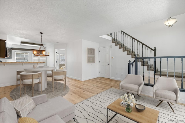 living area with a textured ceiling, stairway, baseboards, and light wood-style floors