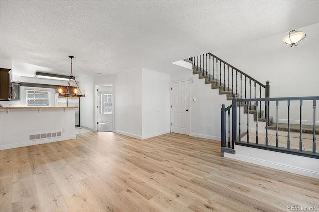 unfurnished living room featuring a textured ceiling, visible vents, baseboards, stairway, and light wood-style floors
