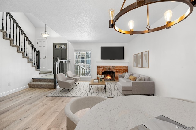 living area featuring a textured ceiling, baseboards, a brick fireplace, wood finished floors, and stairway
