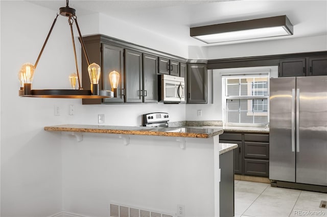 kitchen with a peninsula, light tile patterned flooring, visible vents, a kitchen bar, and appliances with stainless steel finishes