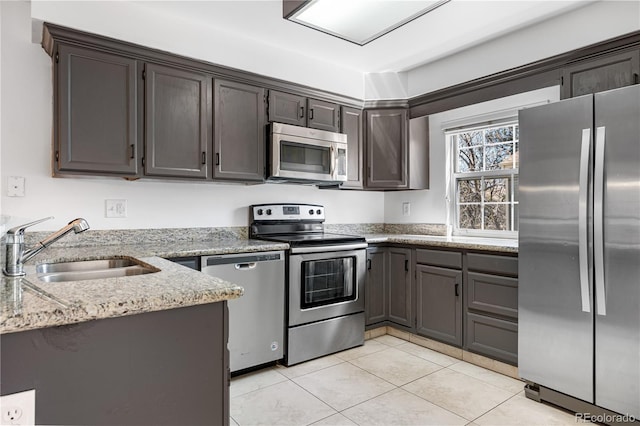 kitchen featuring light stone countertops, light tile patterned floors, dark brown cabinets, a sink, and appliances with stainless steel finishes