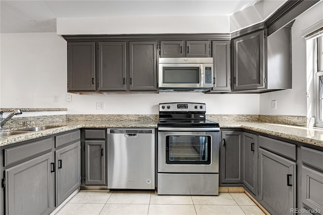 kitchen featuring a sink, light tile patterned floors, light stone countertops, gray cabinetry, and appliances with stainless steel finishes