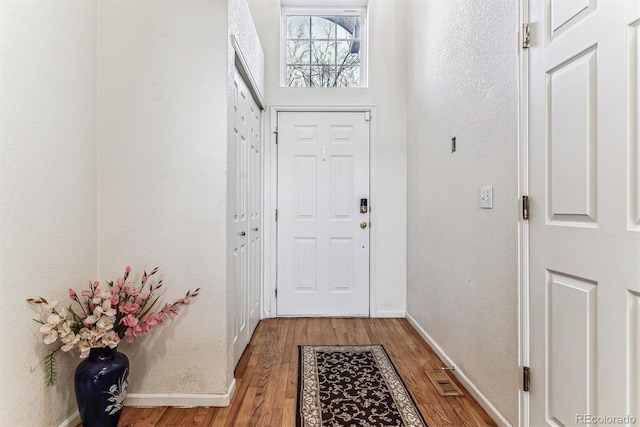 doorway to outside featuring light wood-type flooring, visible vents, a textured wall, and baseboards