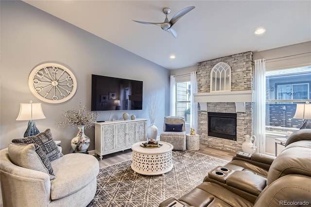 living room featuring hardwood / wood-style flooring, ceiling fan, vaulted ceiling, and a stone fireplace