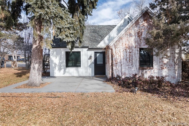 view of front of home with a patio area, board and batten siding, and roof with shingles