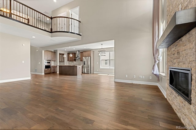 6129 E 143rd Ave, Thornton, CO 80602 - unfurnished living room featuring a towering ceiling, a fireplace, dark wood-style flooring, and a chandelier