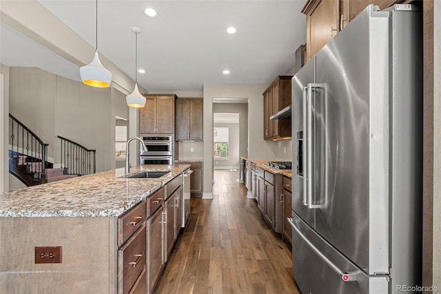 6129 E 143rd Ave, Thornton, CO 80602 - kitchen with appliances with stainless steel finishes, dark wood-style flooring, light stone countertops, recessed lighting, and a kitchen island with sink