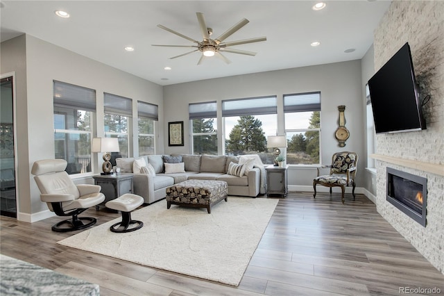 living room featuring ceiling fan, a stone fireplace, and wood-type flooring