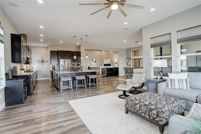 living room with ceiling fan with notable chandelier and light hardwood / wood-style floors