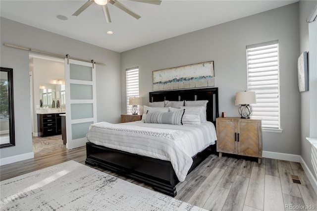 bedroom featuring connected bathroom, a barn door, ceiling fan, and multiple windows