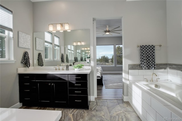 bathroom featuring ceiling fan, a relaxing tiled tub, vanity, and a wealth of natural light