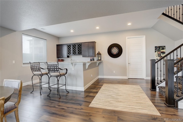 kitchen with dark brown cabinetry, dark wood-type flooring, a kitchen breakfast bar, kitchen peninsula, and a textured ceiling