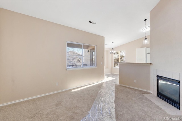 unfurnished living room featuring a tile fireplace, light carpet, a chandelier, and vaulted ceiling