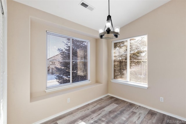 unfurnished dining area featuring wood-type flooring, vaulted ceiling, and a notable chandelier