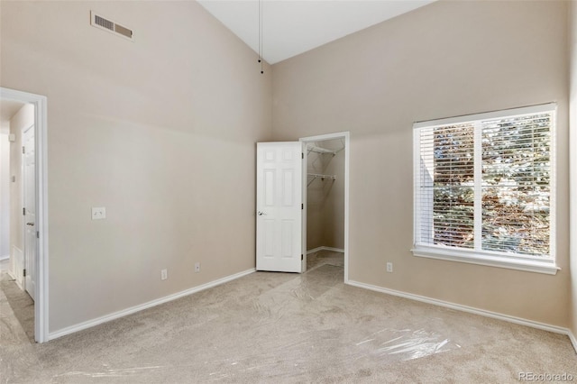 unfurnished bedroom featuring light colored carpet, a walk in closet, high vaulted ceiling, and a closet