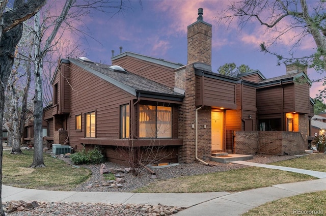 view of front facade featuring brick siding, a chimney, and central AC