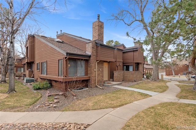 multi unit property featuring a chimney, a front lawn, central AC, and brick siding