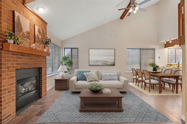 living area featuring a brick fireplace, baseboards, a textured ceiling, high vaulted ceiling, and a ceiling fan