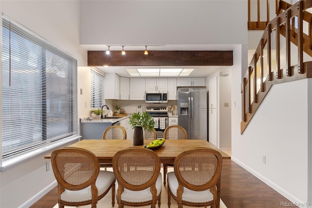 dining area featuring baseboards, beam ceiling, wood finished floors, and rail lighting