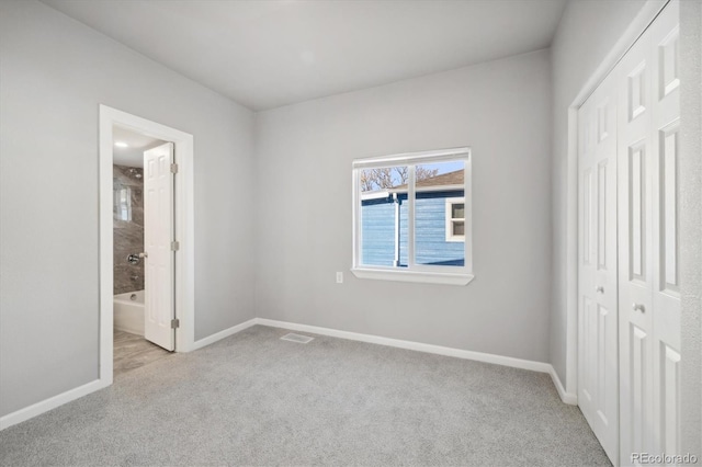 unfurnished bedroom with ensuite bathroom, light carpet, and a closet