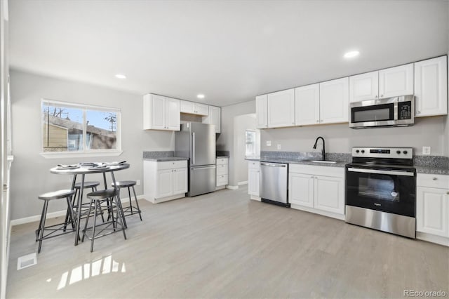 kitchen featuring stainless steel appliances, sink, stone countertops, light hardwood / wood-style flooring, and white cabinetry