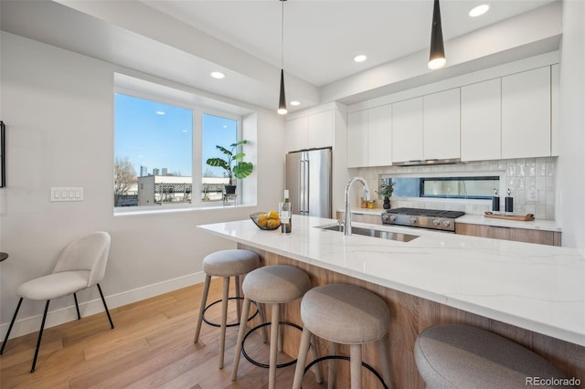kitchen with high end fridge, a breakfast bar area, baseboards, a sink, and white cabinetry