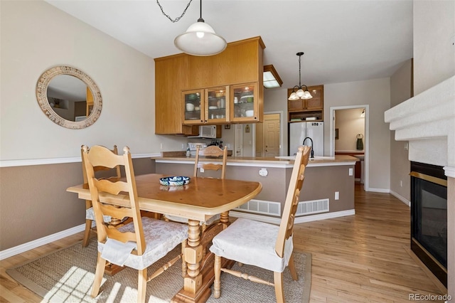 dining area featuring light wood-type flooring, a chandelier, baseboards, and a glass covered fireplace