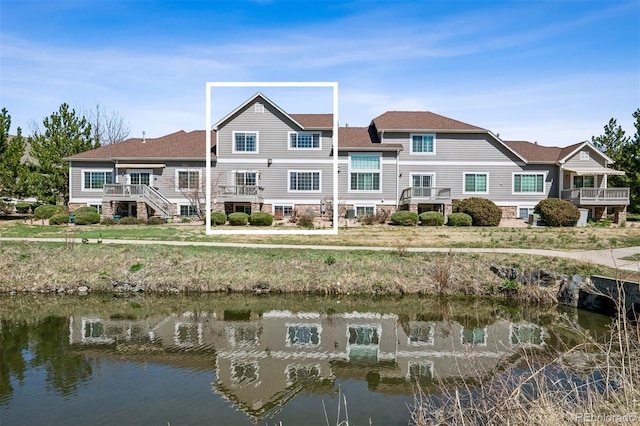 back of property with a water view and a shingled roof