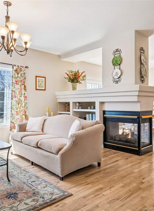 living area featuring light wood finished floors, a chandelier, and a multi sided fireplace