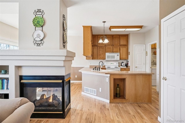 kitchen with white appliances, a sink, light wood-type flooring, and brown cabinetry
