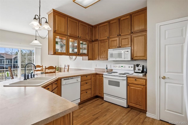 kitchen featuring white appliances, a sink, light wood-type flooring, light countertops, and decorative light fixtures