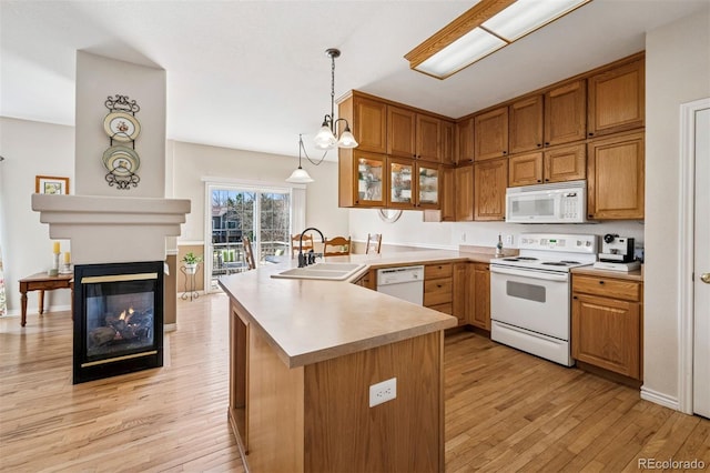 kitchen featuring white appliances, a sink, a peninsula, light wood-style flooring, and brown cabinets
