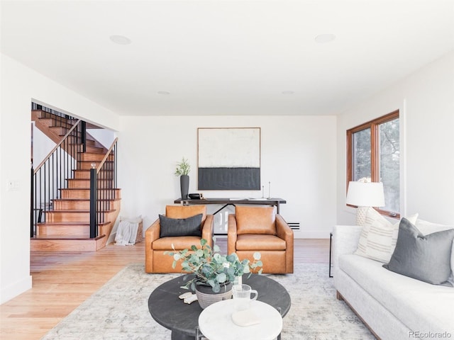 living area featuring a baseboard heating unit, light wood-type flooring, stairway, and baseboards