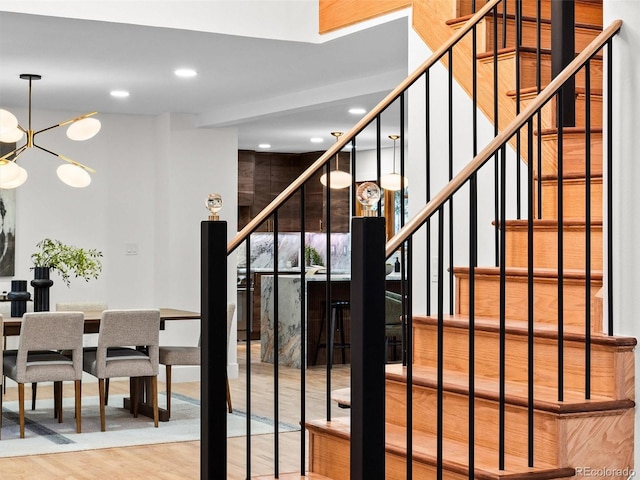 stairs with recessed lighting, wood finished floors, and an inviting chandelier