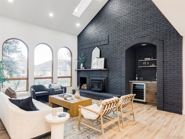 living room with high vaulted ceiling, wine cooler, light wood-style floors, a brick fireplace, and a bar