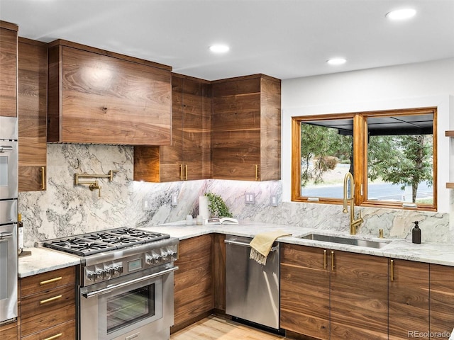 kitchen featuring light stone counters, stainless steel appliances, a sink, backsplash, and modern cabinets