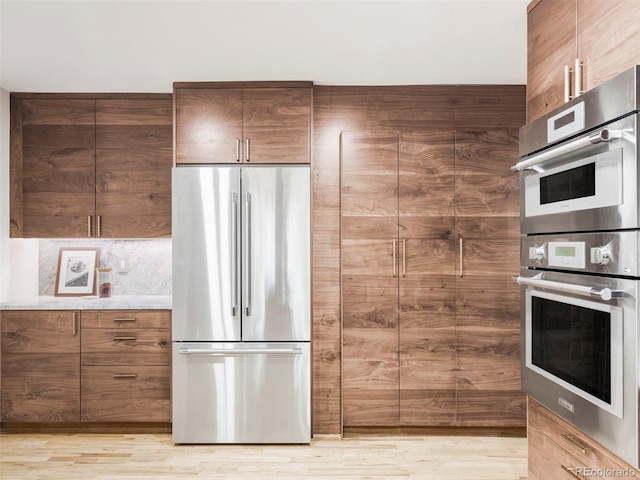 kitchen featuring tasteful backsplash, brown cabinetry, stainless steel appliances, light countertops, and light wood-type flooring